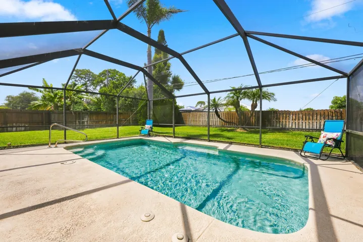 Screened-in swimming pool with a concrete deck, integrated steps, and a handrail
