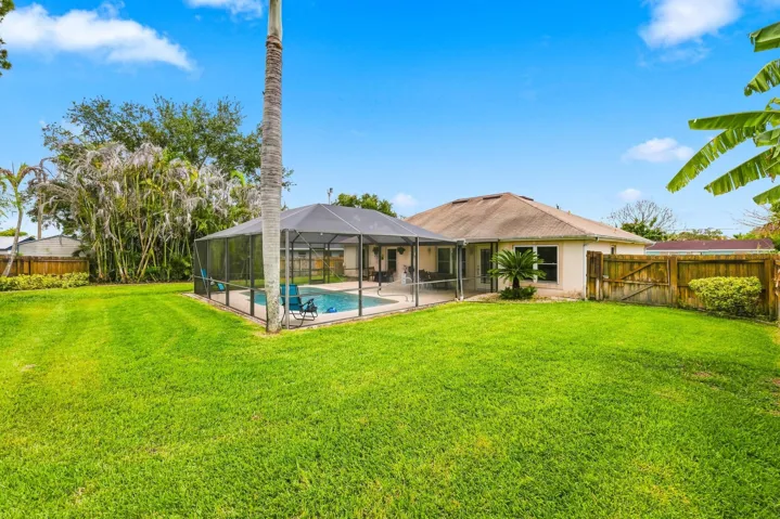 Expansive backyard featuring a meticulously manicured lawn with mature landscaping, including palm and banana trees