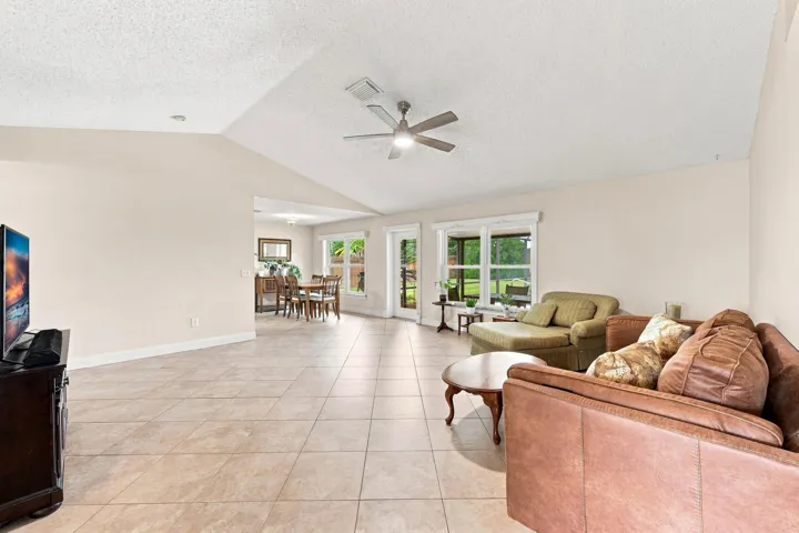 Spacious living area featuring neutral tile flooring, vaulted ceilings, and a ceiling fan