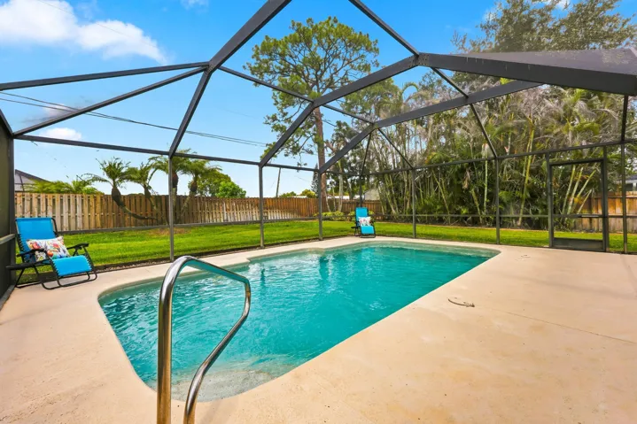 Screened pool enclosure featuring a sport pool, concrete pool deck, and a safety handrail