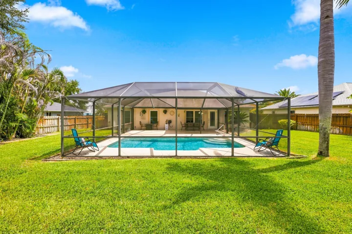 Screened-in swimming pool with a surrounding concrete patio, set against a stucco exterior with multiple glass doors