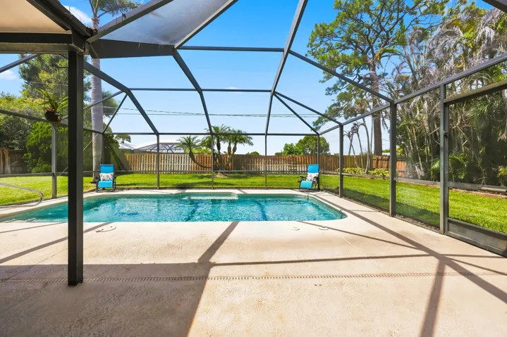 Screened-in outdoor pool area featuring a blue-tiled swimming pool and a light-colored concrete surround