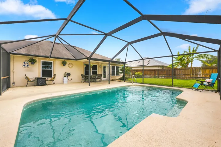 Resort-style pool enclosure featuring a sparkling pool with custom hardscape decking, expansive screened lanai with high vaulted ceiling, and direct access to the home's covered patio area