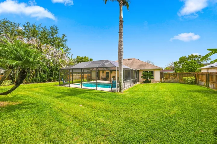 Expansive lawn featuring a screened pool enclosure and mature palm trees