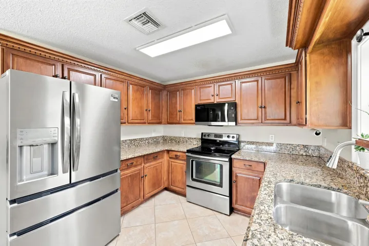 Kitchen featuring extensive wood cabinetry with crown molding, granite-finish countertops, and stainless steel appliances including a double-door refrigerator, range, and microwave