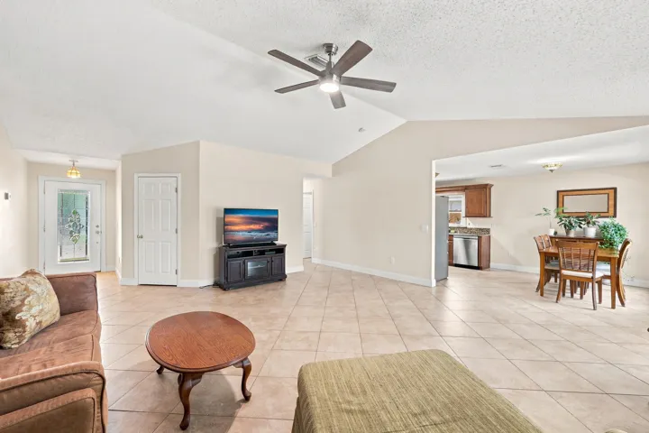 Open-concept living area featuring neutral-toned tile flooring, vaulted ceilings, and a ceiling fan