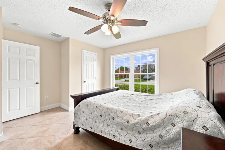 Bedroom featuring tile flooring, neutral wall paint, a ceiling fan with integrated lighting, and multiple windows