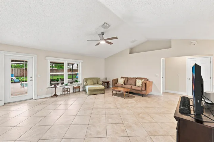 Spacious living area featuring large format tile flooring, vaulted ceilings, and a ceiling fan