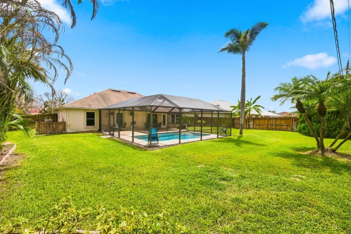 Expansive backyard featuring a screened-in swimming pool with a surrounding paved deck, mature palm trees, and perimeter fencing