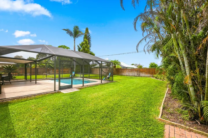 Expansive backyard featuring a screened-in pool enclosure, concrete pool deck, and a lush lawn