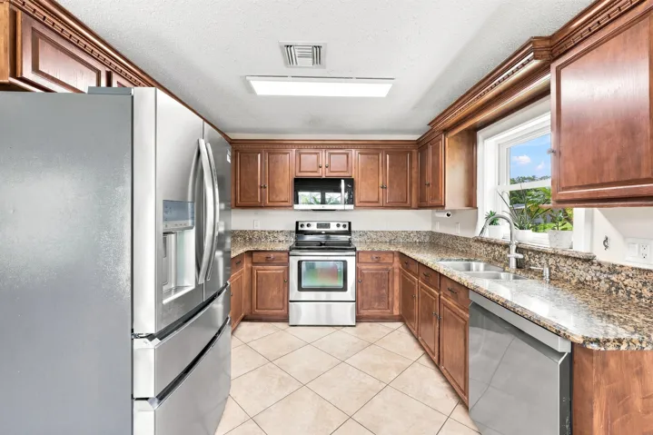 Kitchen featuring wood cabinetry, granite countertops, stainless steel appliances, a double basin sink, and tile flooring