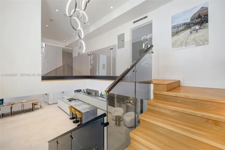 A floating staircase with glass railings overlooks the dramatic living spaces below, connecting both levels with contemporary elegance.