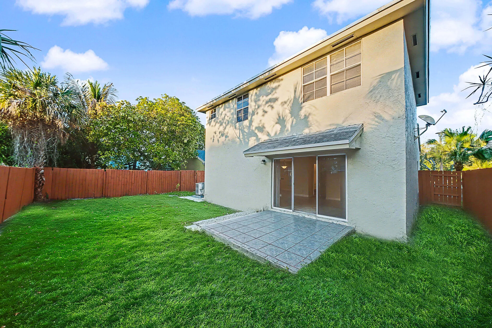 Expansive grassy backyard featuring a tiled patio and sliding glass doors