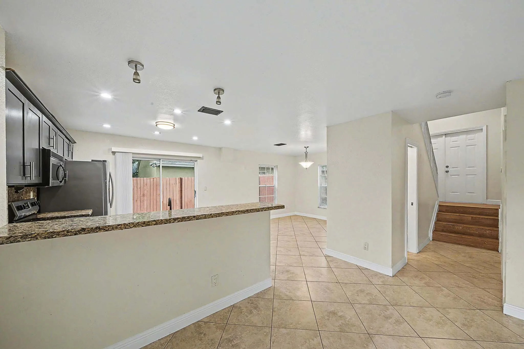 Open-concept living space featuring a breakfast bar with a granite-style countertop, dark wood-finish cabinetry, stainless steel appliances, and sliding glass doors to the exterior