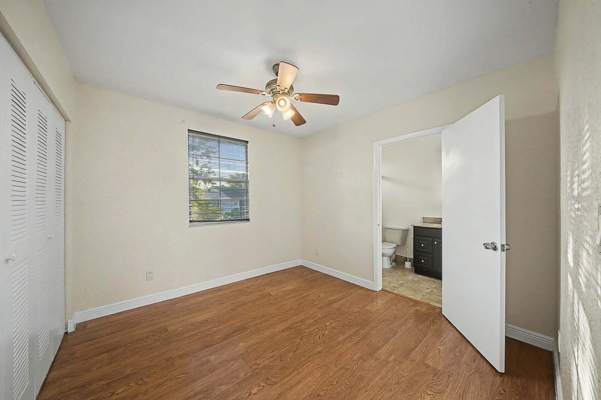Bedroom featuring wood-finish flooring, a ceiling fan with integrated lighting, and a window with blinds