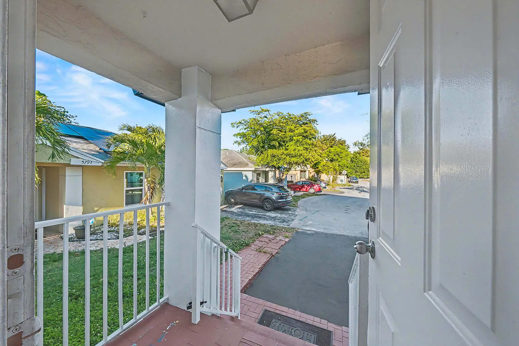 Covered front entry with white panel door and metal railing, featuring brick-patterned flooring