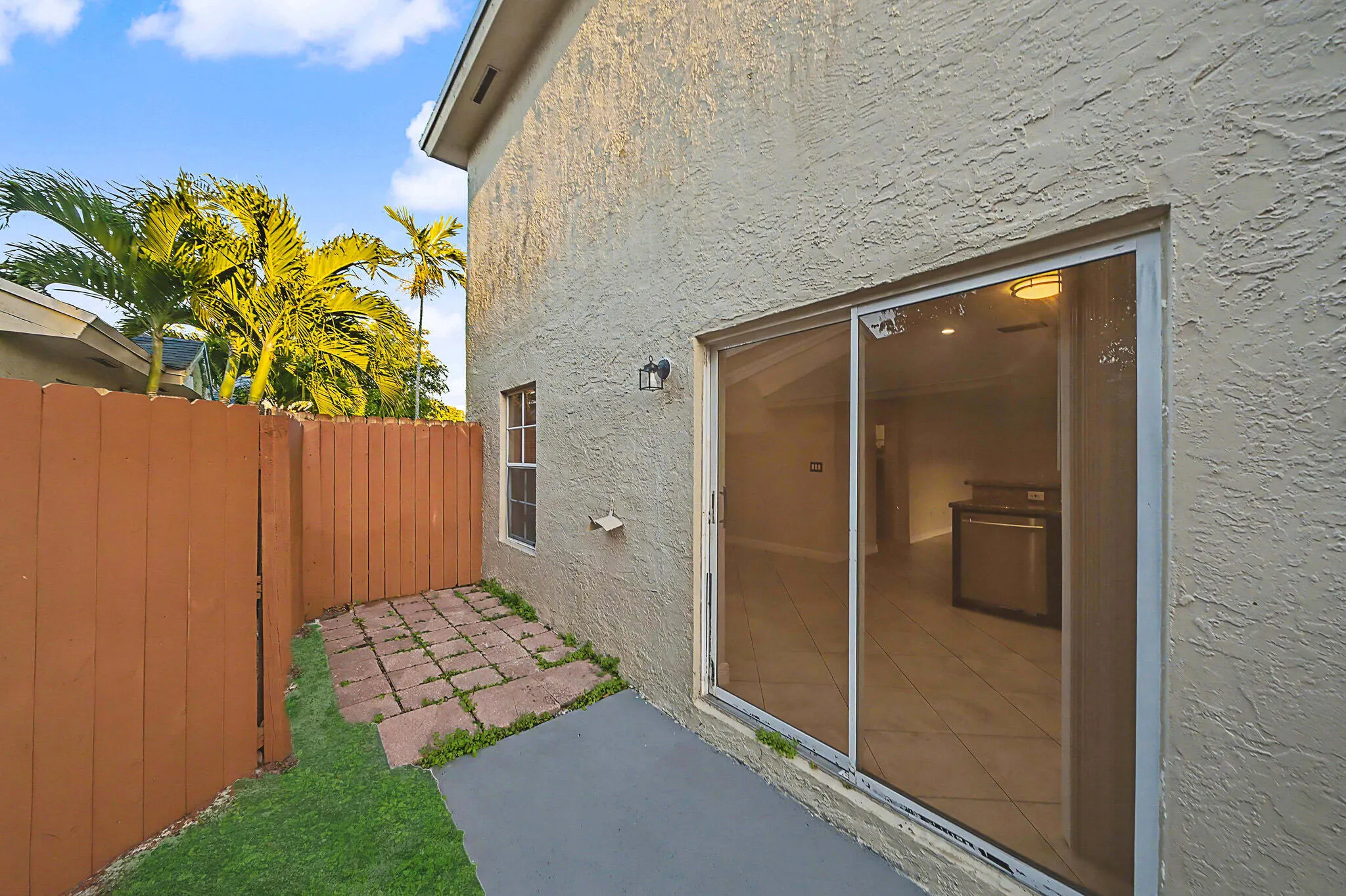 Outdoor patio with stucco exterior, sliding glass door, privacy fencing, and mature palm trees