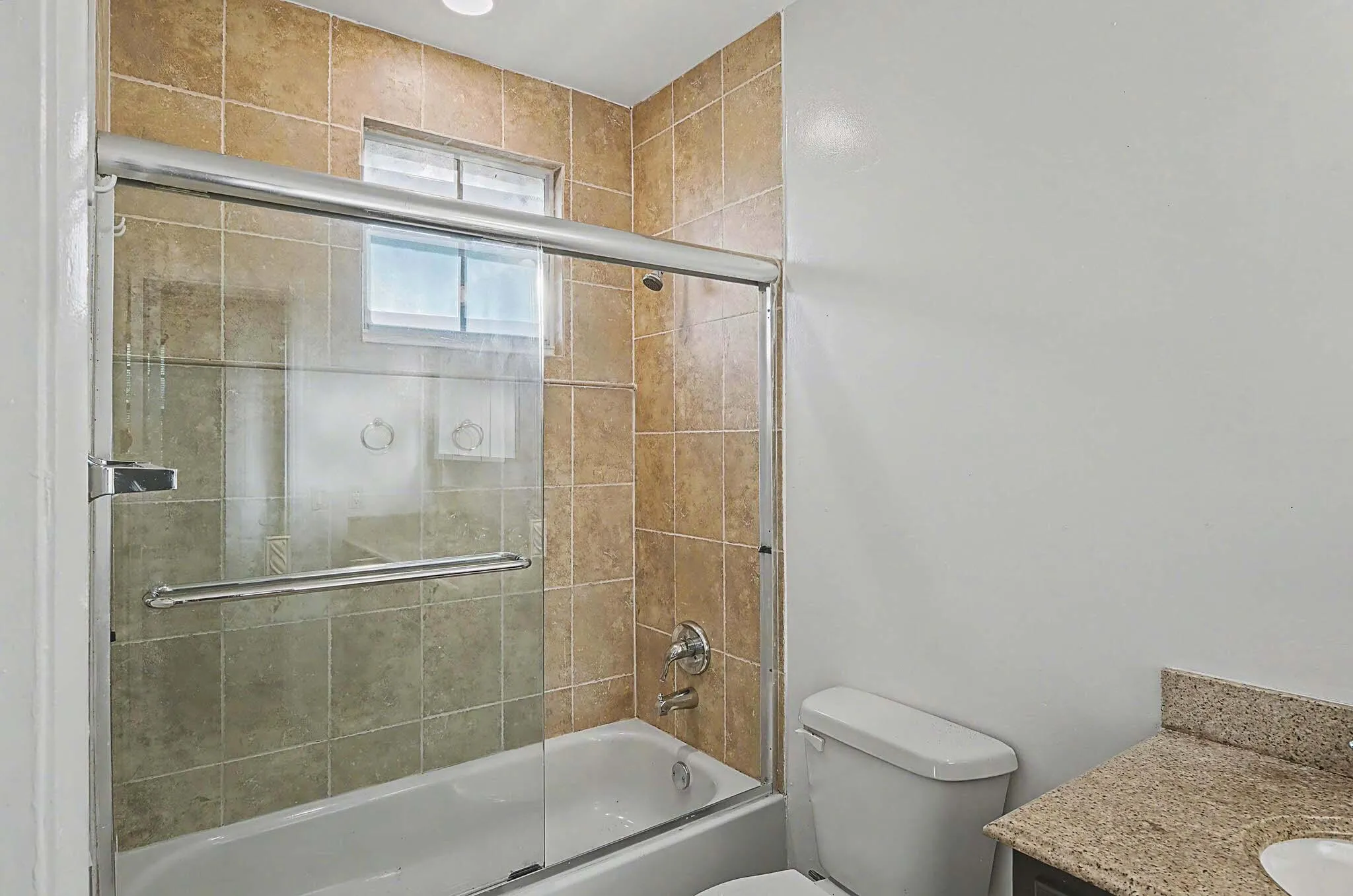Bathroom featuring a tiled tub-shower combination with sliding glass doors, a transom window, and a vanity with a granite countertop