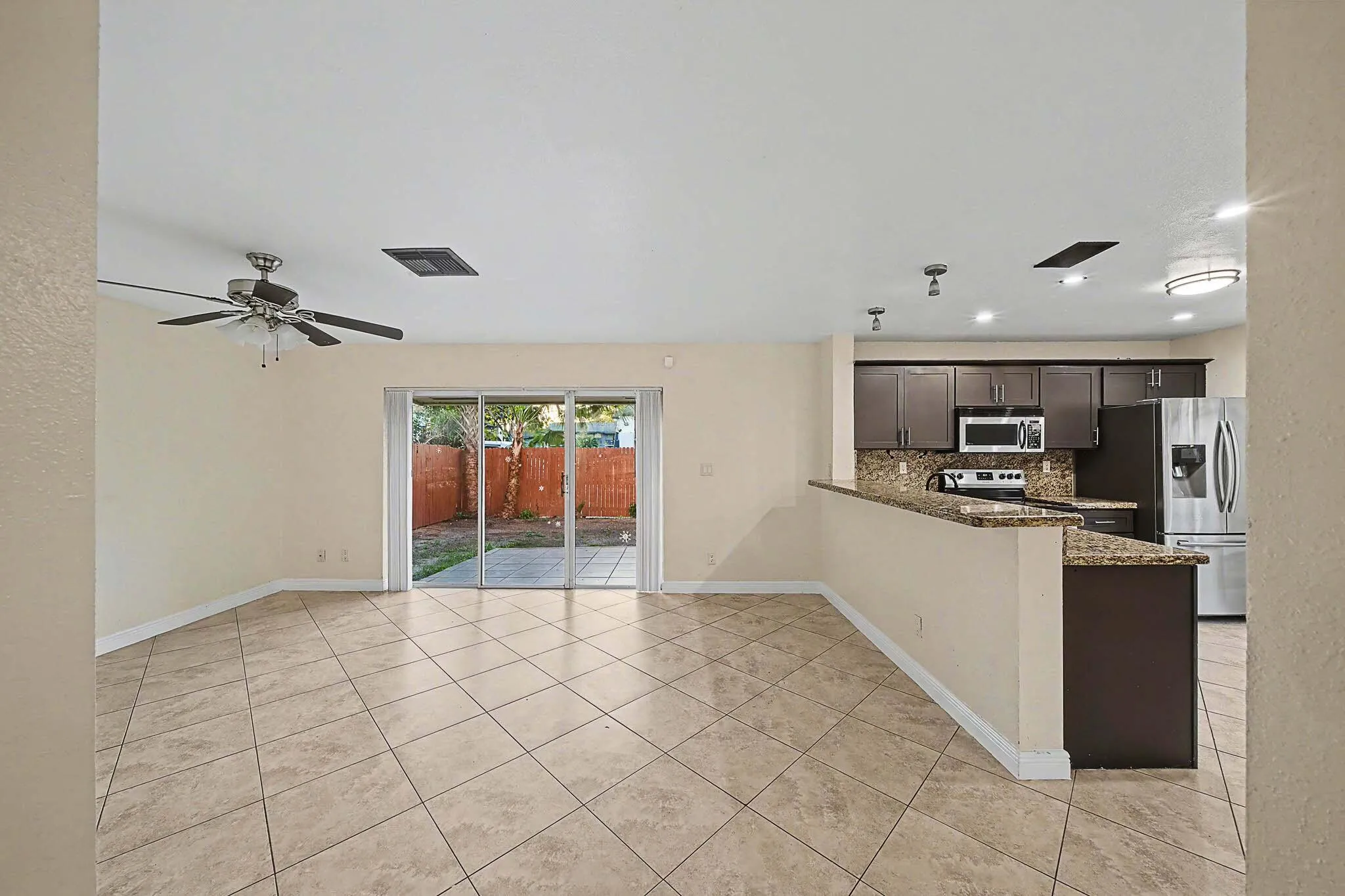 Spacious living area featuring tile flooring, a ceiling fan, and sliding glass doors opening to a fenced patio