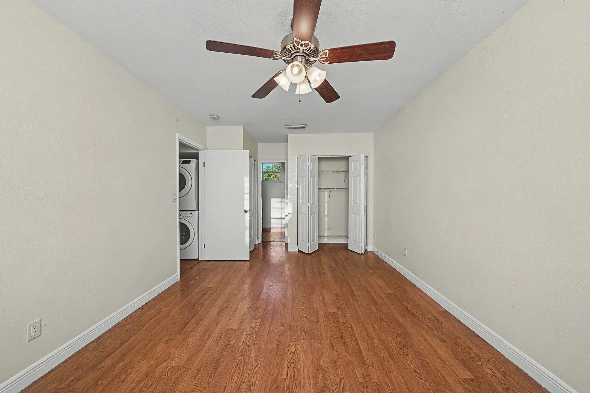 Spacious interior room with wood-finish flooring, ceiling fan with integrated lighting, and white baseboards