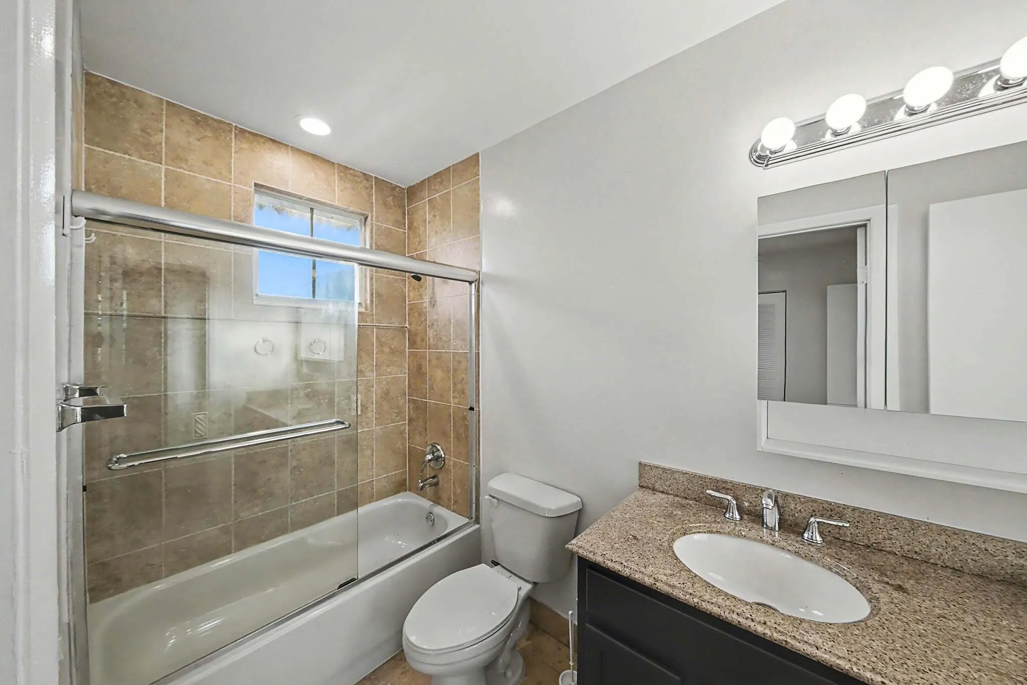 Bathroom featuring a tiled shower/tub combination with glass doors, a vanity with a granite-style countertop, an oval undermount sink, and chrome fixtures
