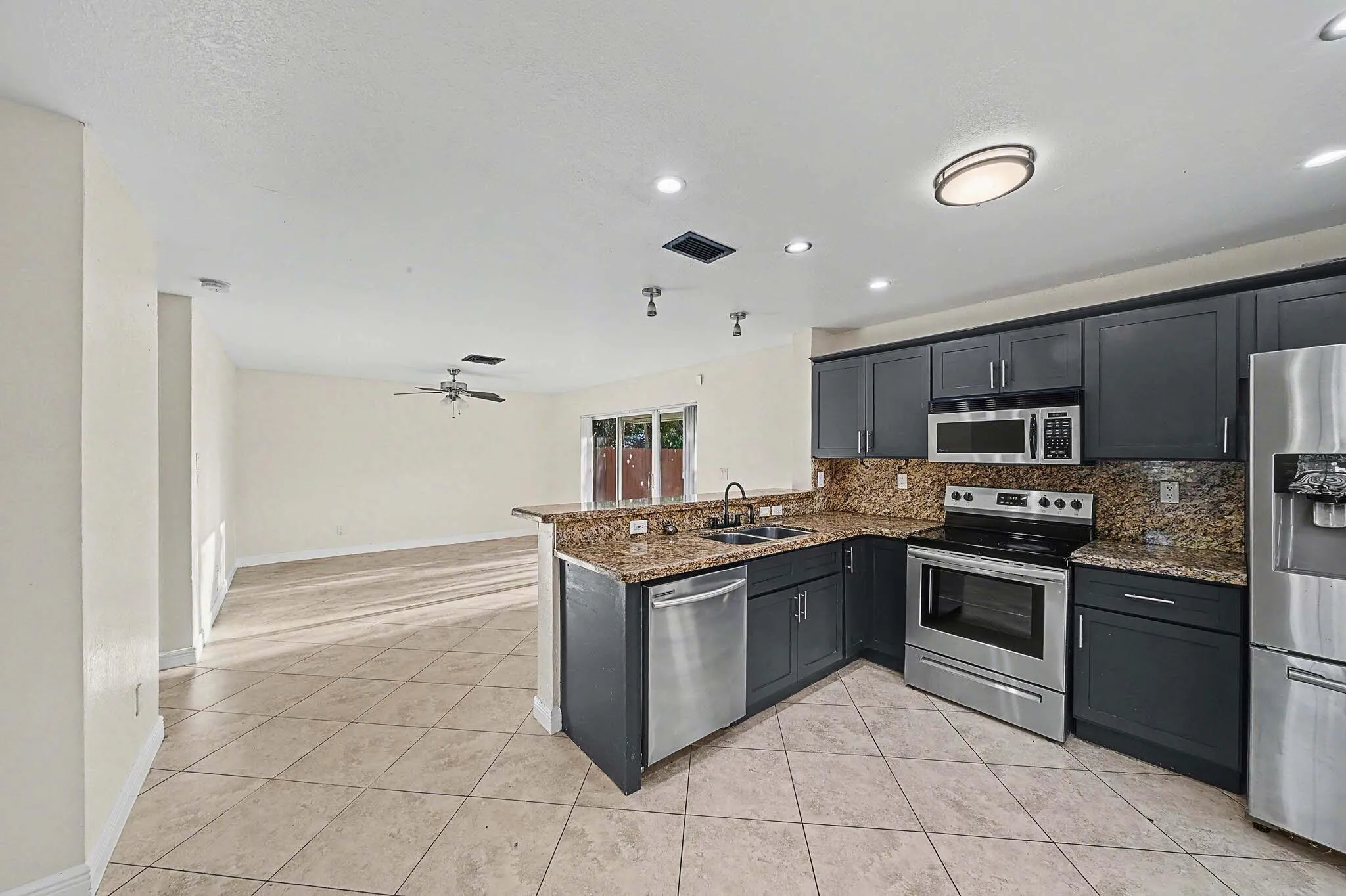 Kitchen featuring dark wood cabinetry, stainless steel appliances, speckled stone countertops, and a coordinating stone backsplash