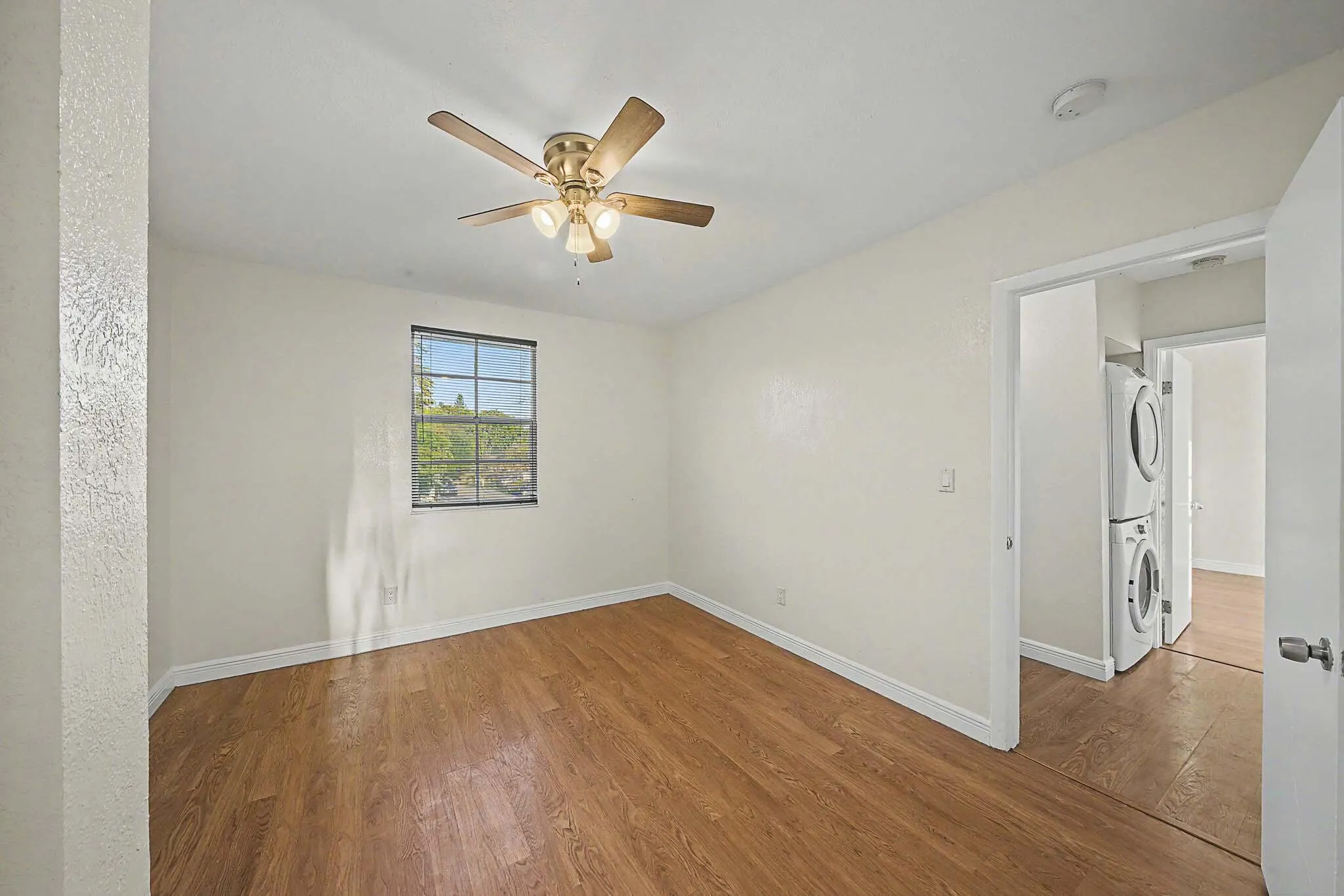 Room featuring wood-finish flooring, a window with exterior views, and a ceiling fan with integrated lighting