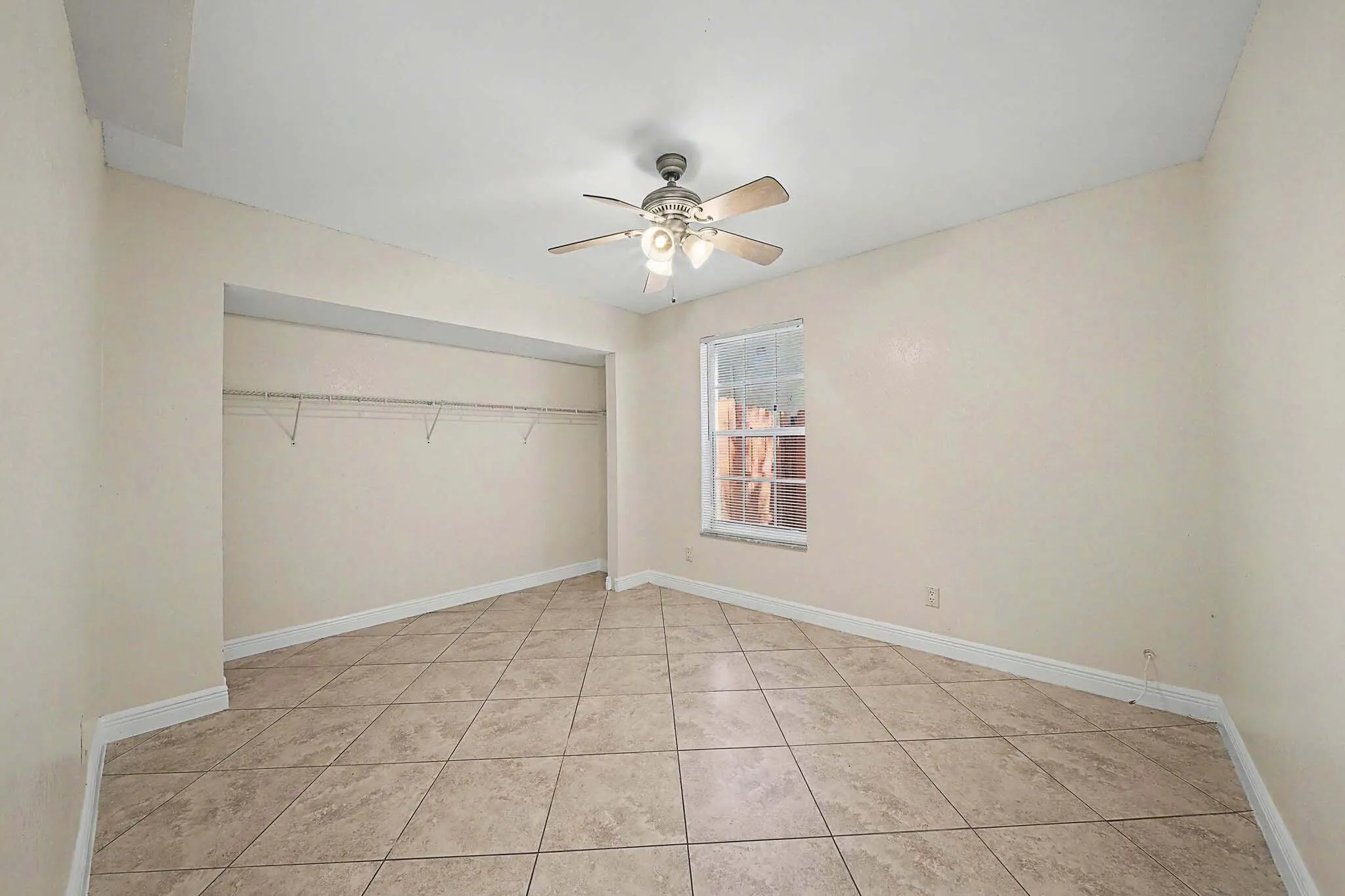 Spacious room featuring neutral-toned walls, diagonal tile flooring, and a ceiling fan with integrated lighting