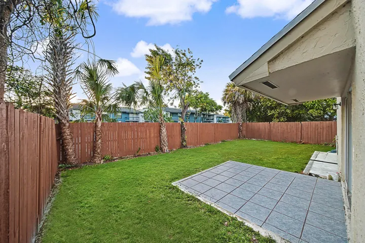 Expansive backyard oasis featuring a lush, manicured lawn, mature palm and native trees, and a generous paved patio area adjoining the home