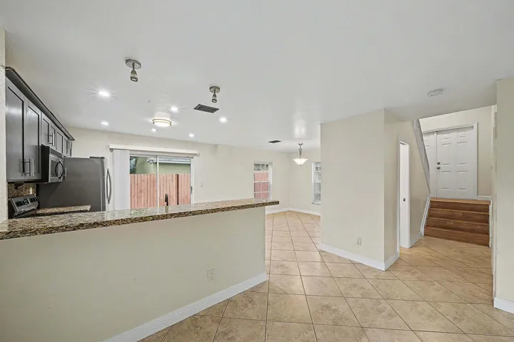 Open-concept living space featuring a breakfast bar with a granite-style countertop, dark wood-finish cabinetry, stainless steel appliances, and sliding glass doors to the exterior