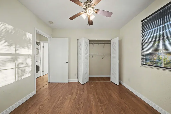 Room featuring wood-finish flooring, a ceiling fan with integrated lighting, and a window with horizontal blinds