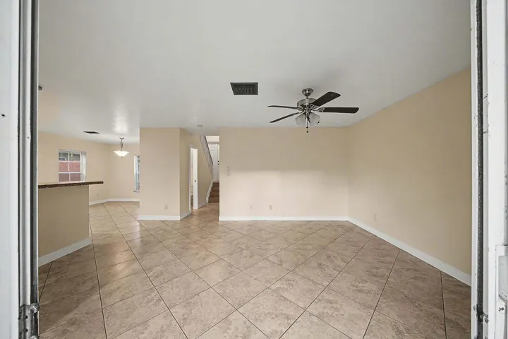 Spacious living area featuring neutral-toned walls, diagonal tile flooring, and a ceiling fan with light fixture