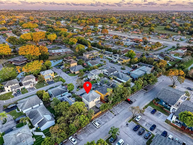 Aerial perspective highlighting the property within a residential setting, featuring surrounding mature trees and nearby bodies of water