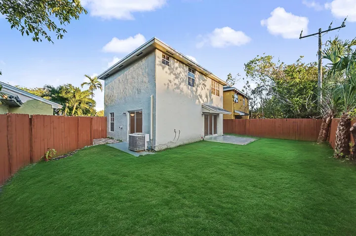 Expansive green lawn framed by a privacy fence, offering a concrete patio and a stucco exterior with multiple windows