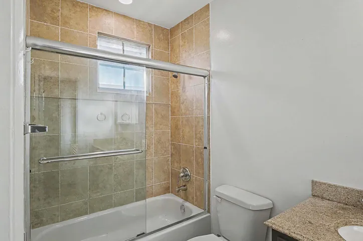 Bathroom featuring a tiled tub-shower combination with sliding glass doors, a transom window, and a vanity with a granite countertop