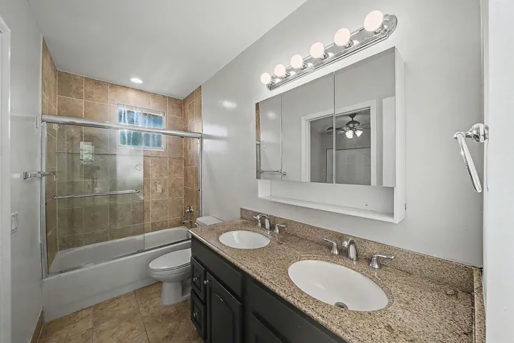 Bathroom featuring a dual sink vanity with a stone-finish countertop, a mirrored medicine cabinet, and a chrome light fixture
