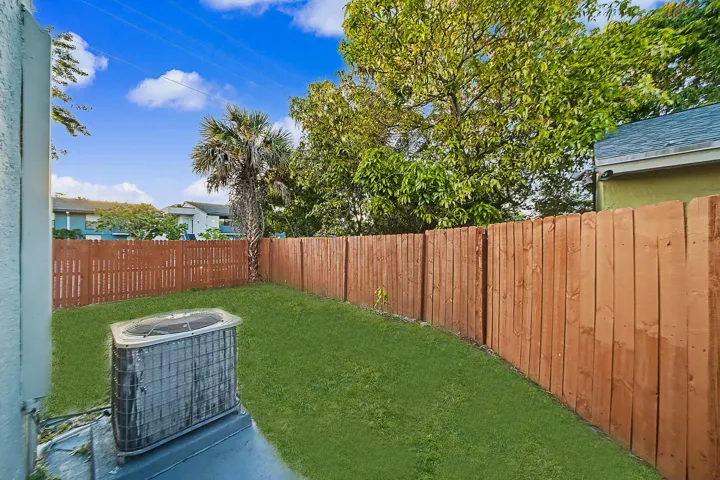 Fenced backyard featuring a manicured lawn, established trees, and a palm tree