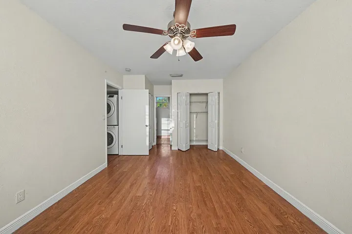 Spacious interior room with wood-finish flooring, ceiling fan with integrated lighting, and white baseboards