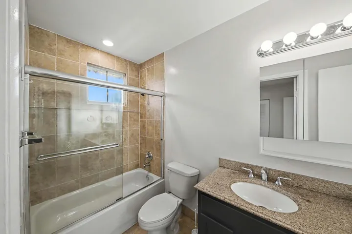 Bathroom featuring a tiled shower/tub combination with glass doors, a vanity with a granite-style countertop, an oval undermount sink, and chrome fixtures
