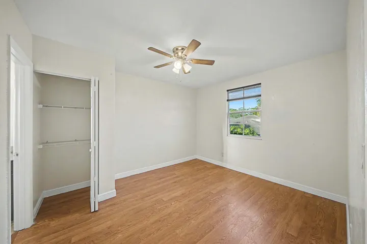 Room featuring wood-finish flooring, a ceiling fan with integrated lighting, and a window with blinds