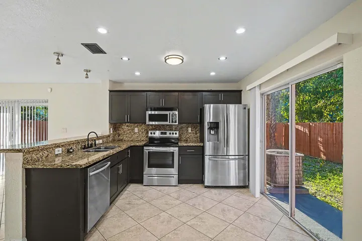 Modern kitchen featuring dark cabinetry, granite countertops, and stainless steel appliances including a refrigerator, range, microwave, and dishwasher