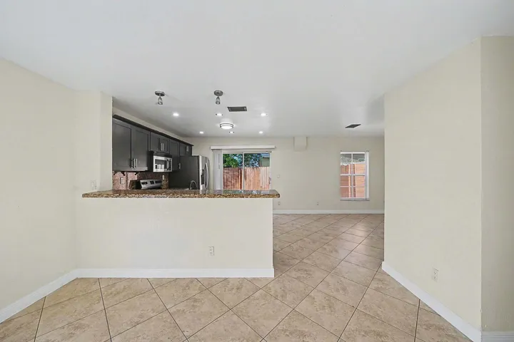 Open-concept living area with neutral tile flooring, a kitchen featuring dark cabinetry, stainless steel appliances, and a granite-look countertop peninsula