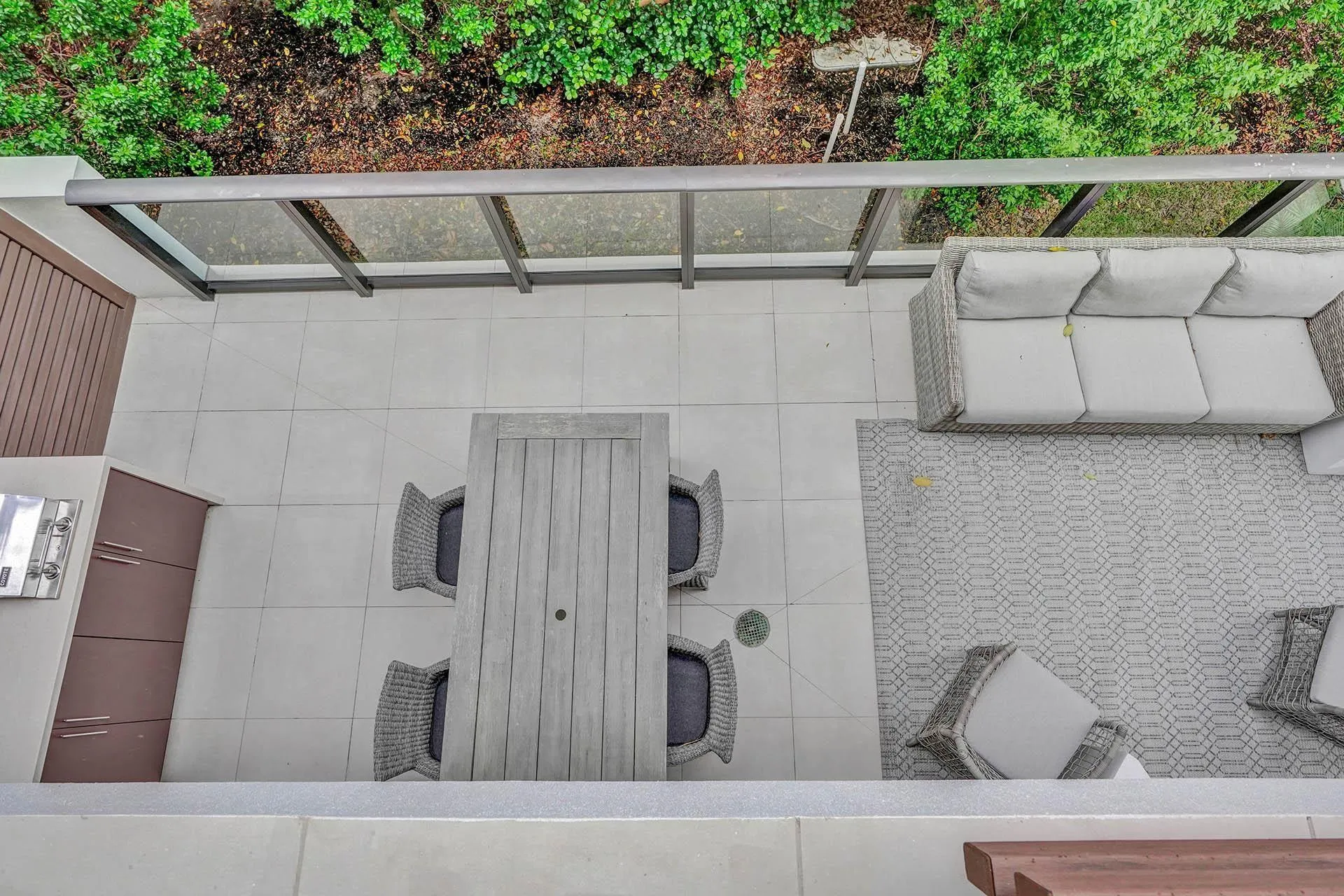 Spacious exterior patio featuring light-toned tile flooring, an integrated built-in grill, and a glass-paneled railing system