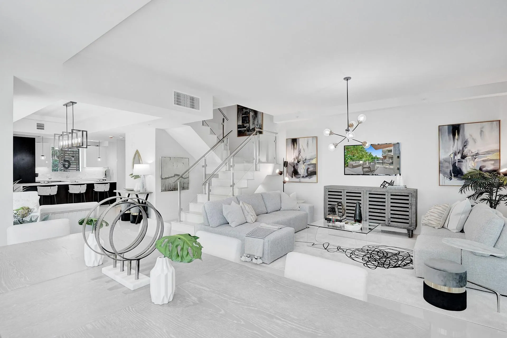 Open-concept living space featuring wood-finish flooring, a contemporary staircase with glass railing, recessed lighting, and a modern kitchen with a large island and pendant lighting