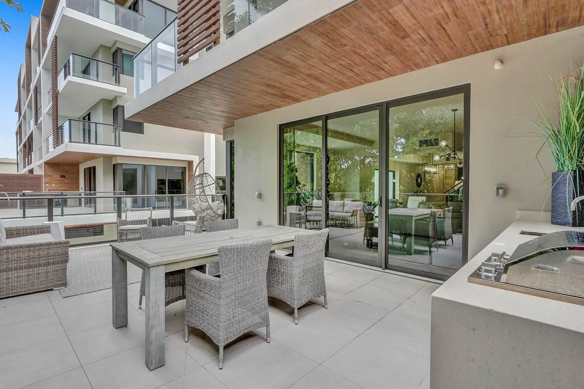Spacious private patio featuring large format tile flooring, an outdoor kitchen with integrated grill, and a wood-finish ceiling accent
