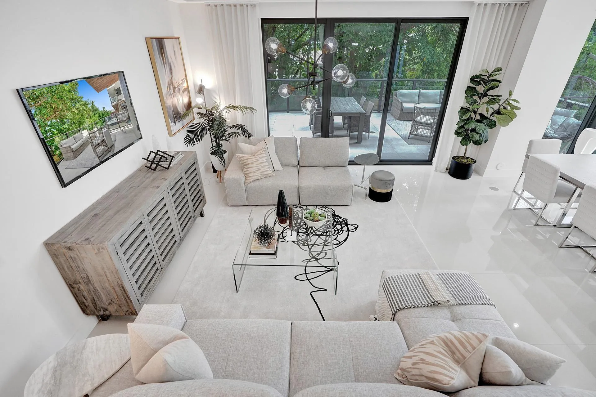 Spacious living area featuring polished light-toned flooring, expansive glass sliding doors leading to an outdoor patio, and a contemporary chandelier