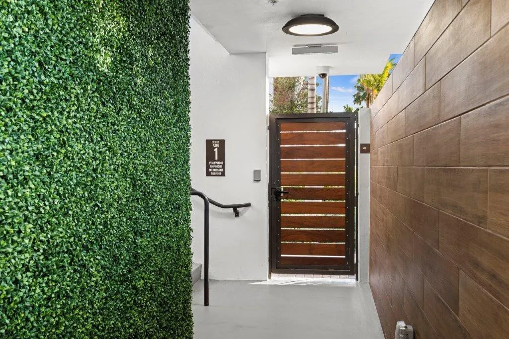 Exterior entryway featuring a faux hedge wall, a wood-slat gate with a metal frame, and wood-finish paneling
