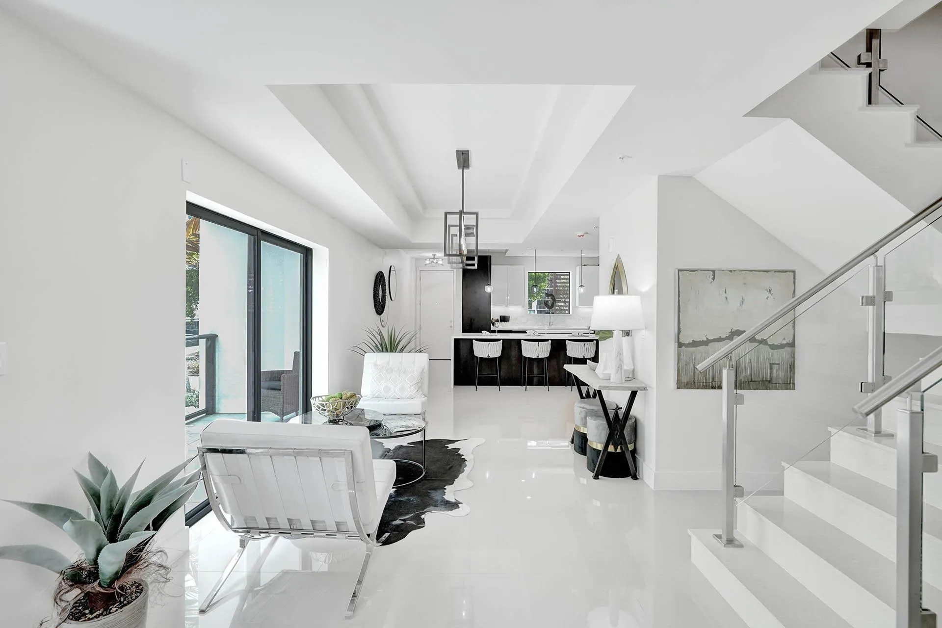 Open-concept interior featuring high ceilings, white tile flooring, and a modern glass and metal staircase