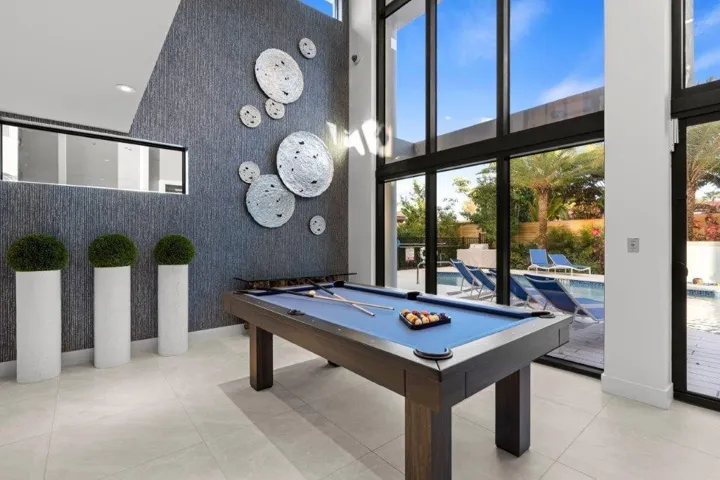Contemporary recreation room featuring a regulation pool table with blue felt surface, polished concrete flooring, and floor-to-ceiling multi-panel glass doors opening to the outdoor entertaining space