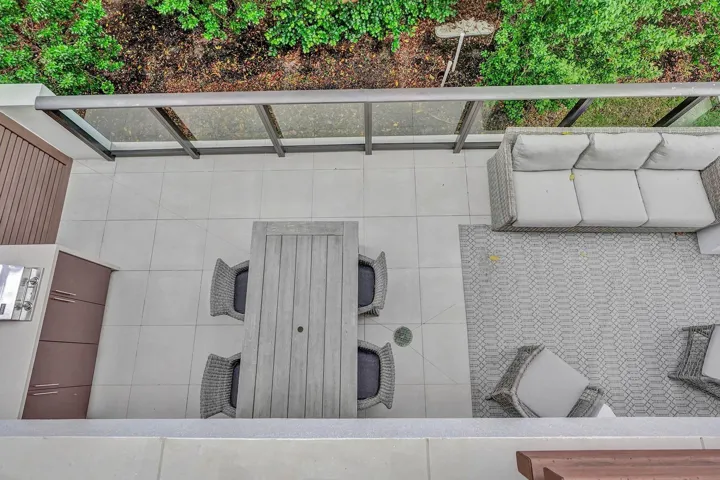 Spacious exterior patio featuring light-toned tile flooring, an integrated built-in grill, and a glass-paneled railing system
